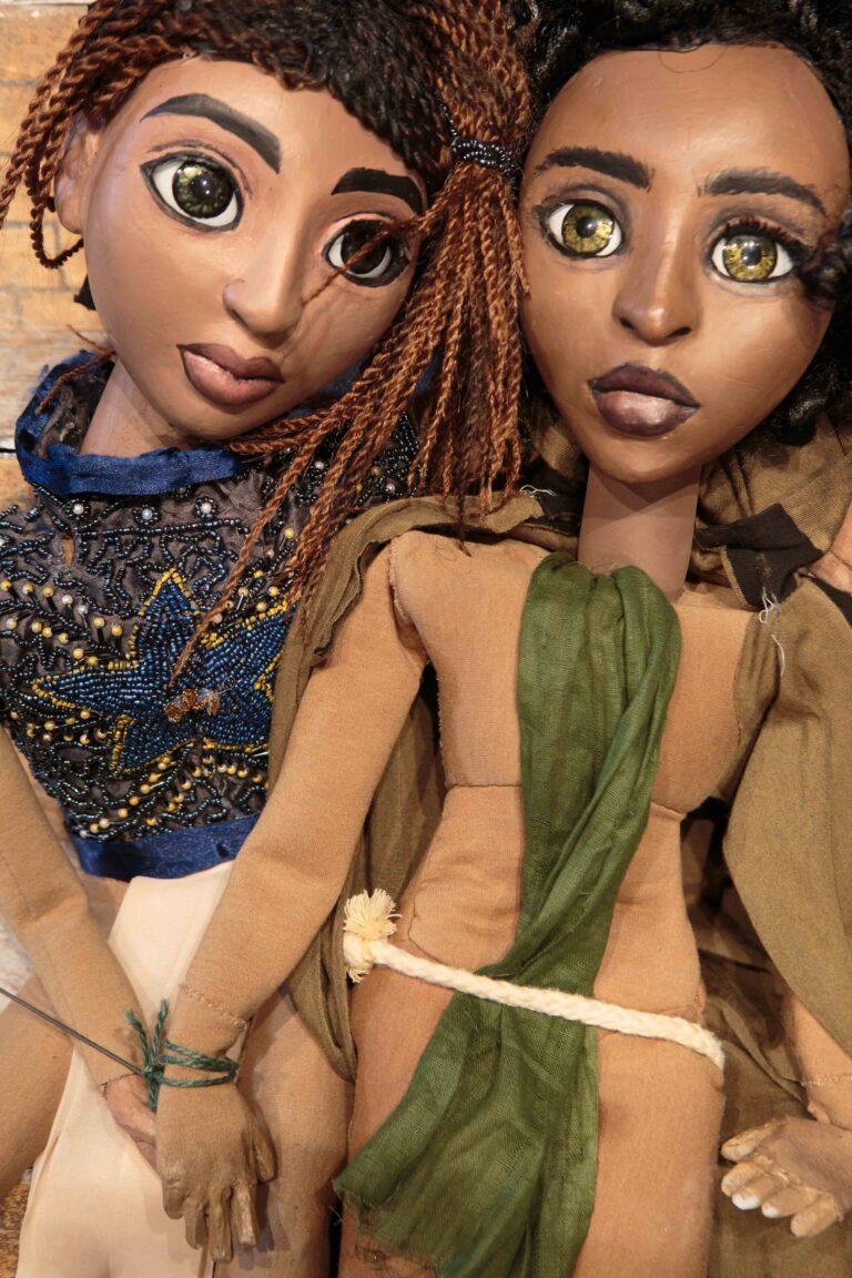 Two tabletop puppets: Astra in a blue beaded stop and Lilt in a green sash and rope belt.