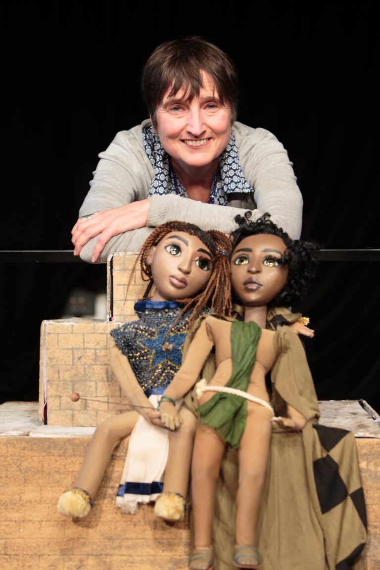 Naomi Foyle posing, smiling, with the two puppets Astra and Lilt