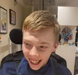 A smiling teenage boy, leaning forward in his wheelchair.